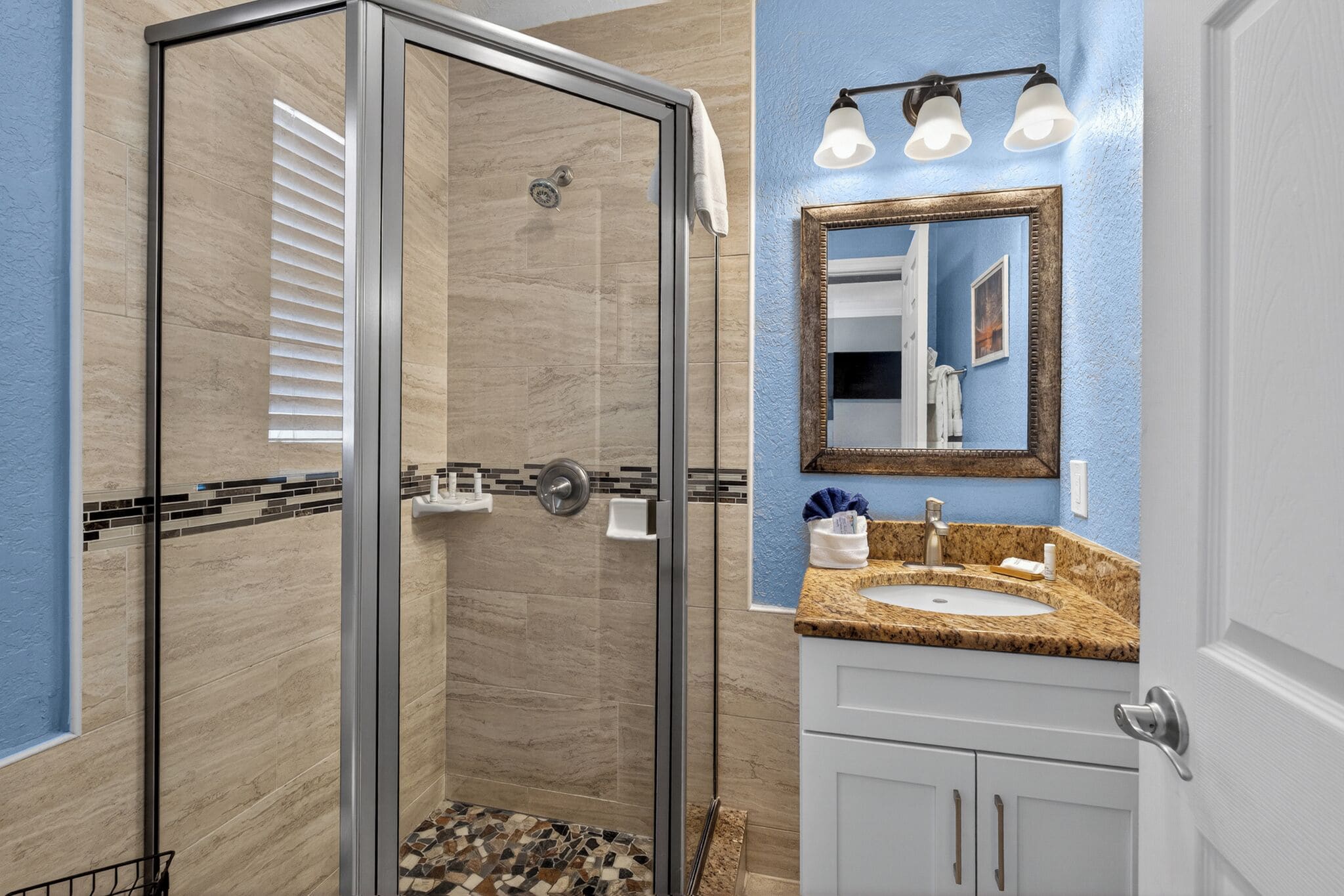A bathroom with a glass-enclosed shower, a sink with a marble countertop, and a mirror with a wooden frame.