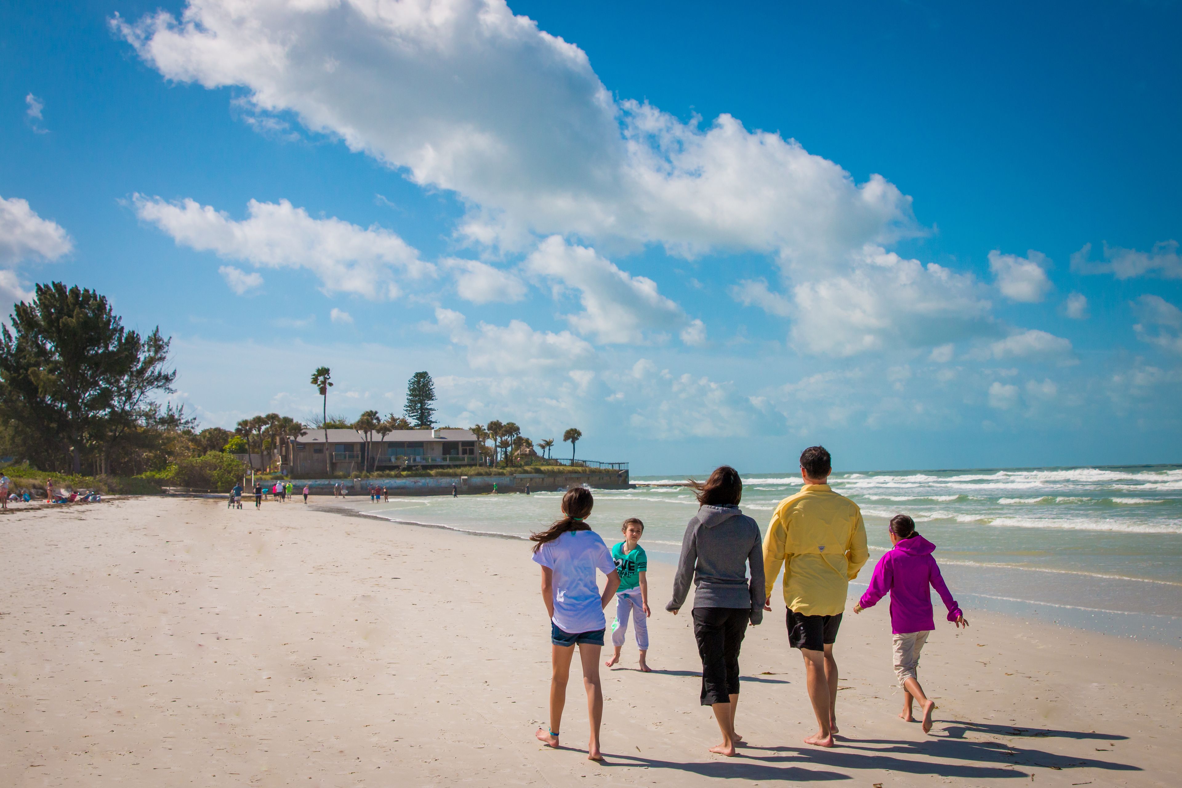 A beach with a clear sky, people walking, and a building in the background.