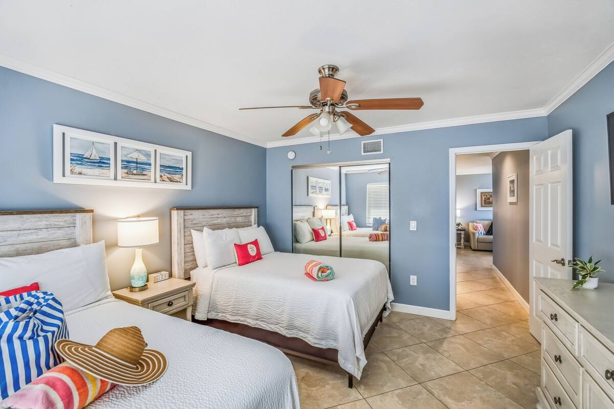 Quarto com duas camas, um ventilador de teto, mesa de cabeceira com luminária e cômoda.