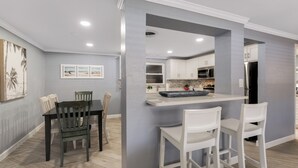 A modern kitchen with white cabinets, a central island, and a dining area with a table and chairs.