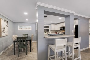 Una cocina moderna con armarios blancos, una isla central y una zona de comedor con una mesa y sillas.