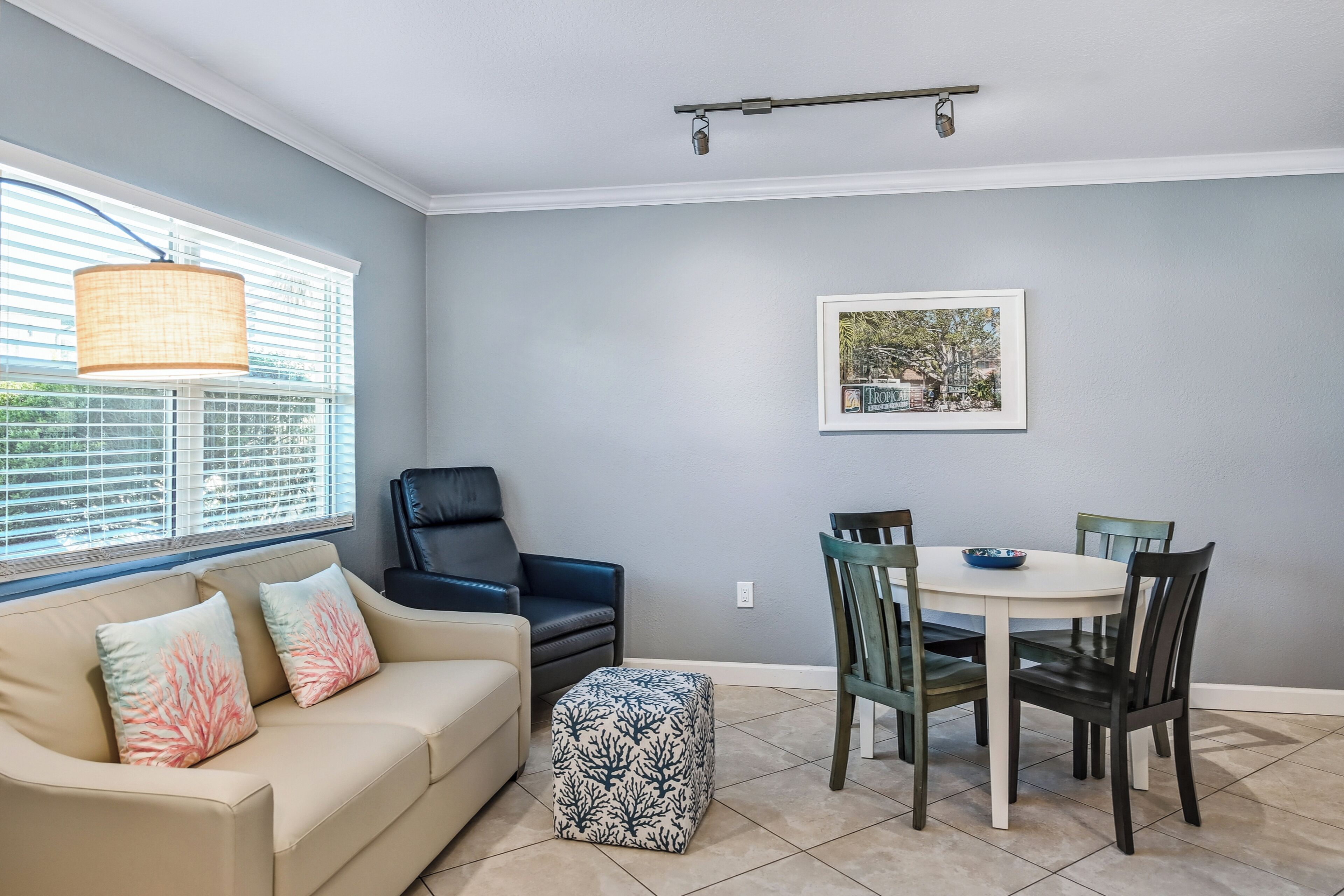 Un coin repas avec une table ronde et des chaises, un canapé agrémenté de coussins décoratifs et une fenêtre avec des stores.