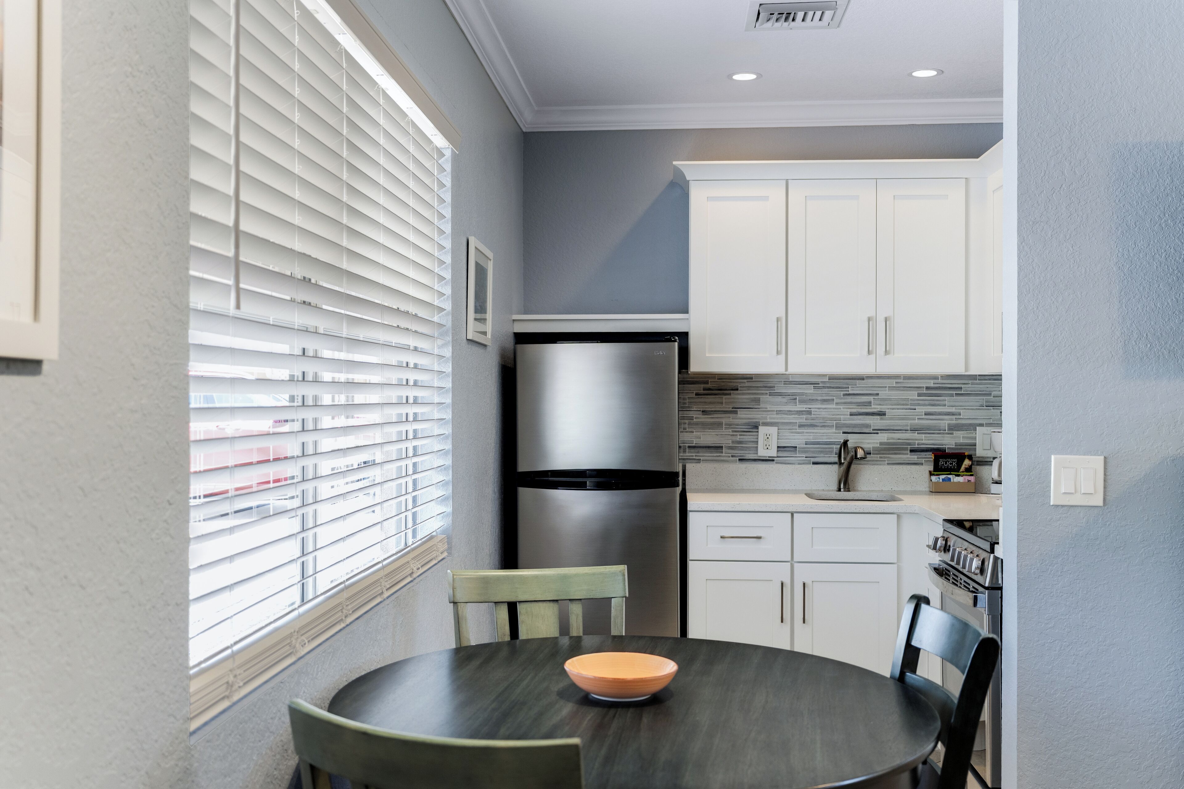 A compact kitchen with white cabinets, a stainless steel refrigerator, and a tiled backsplash.