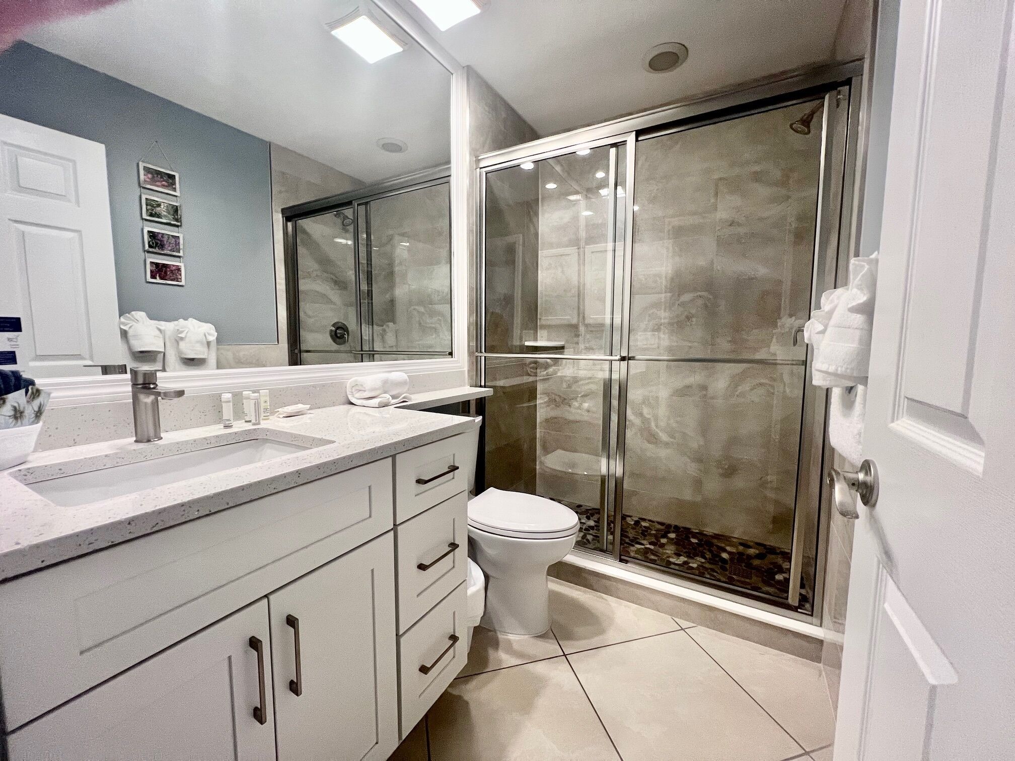 Un baño moderno con cabina de ducha de vidrio, un lavabo blanco con encimera de mármol y un inodoro.