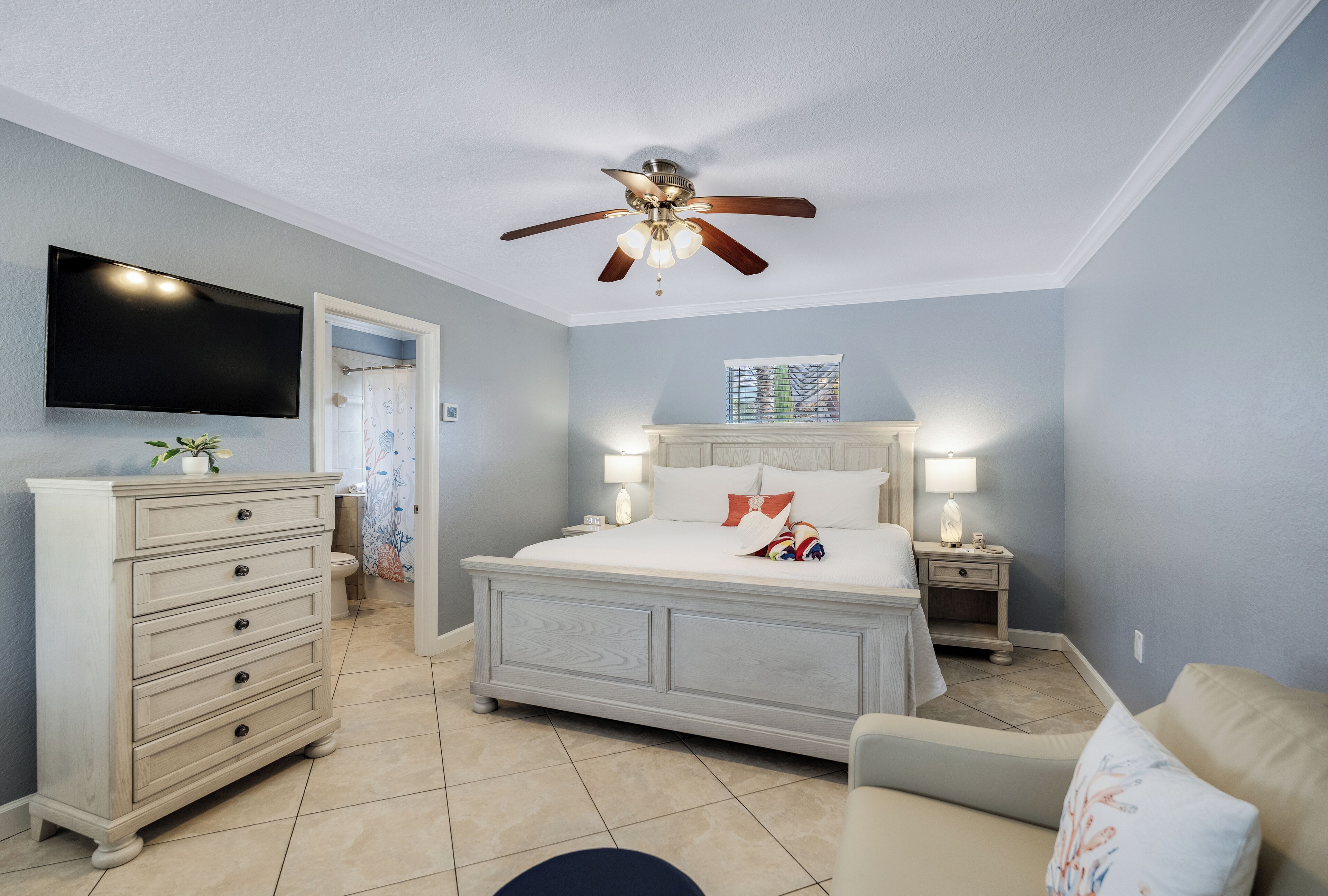 A bedroom with a bed, bedside tables, a TV, a ceiling fan, and a dresser.