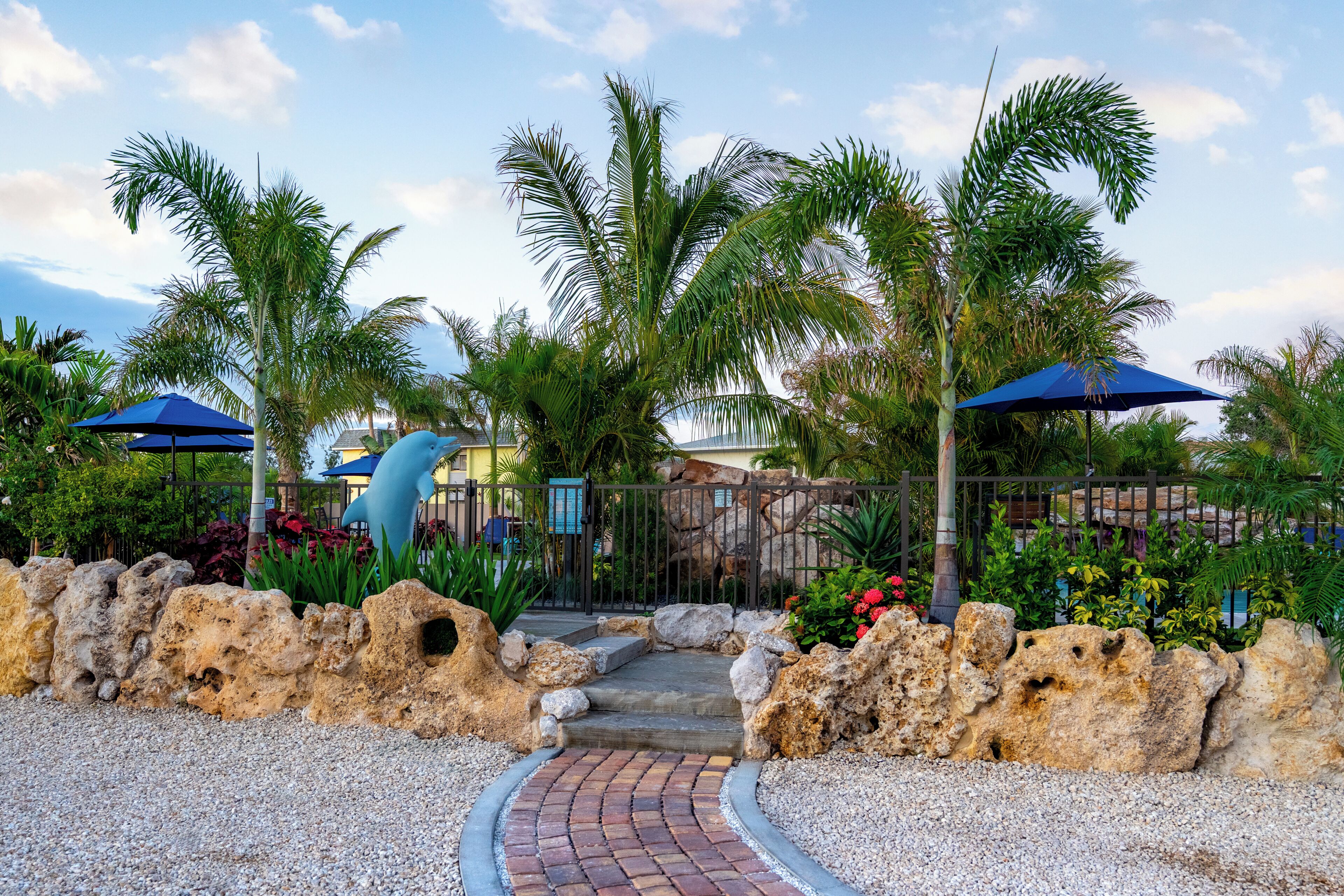 A pathway leading to a building with a rock wall and palm trees.