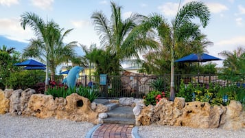 A pathway leading to a building with a rock wall and palm trees.