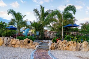 A pathway leading to a building with a rock wall and palm trees.
