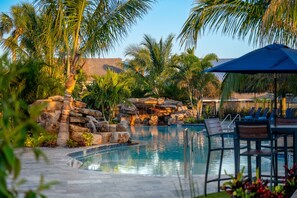A pool area with a waterfall feature, lounge chairs, and palm trees. - Tropical Beach Resorts (Siesta Key)