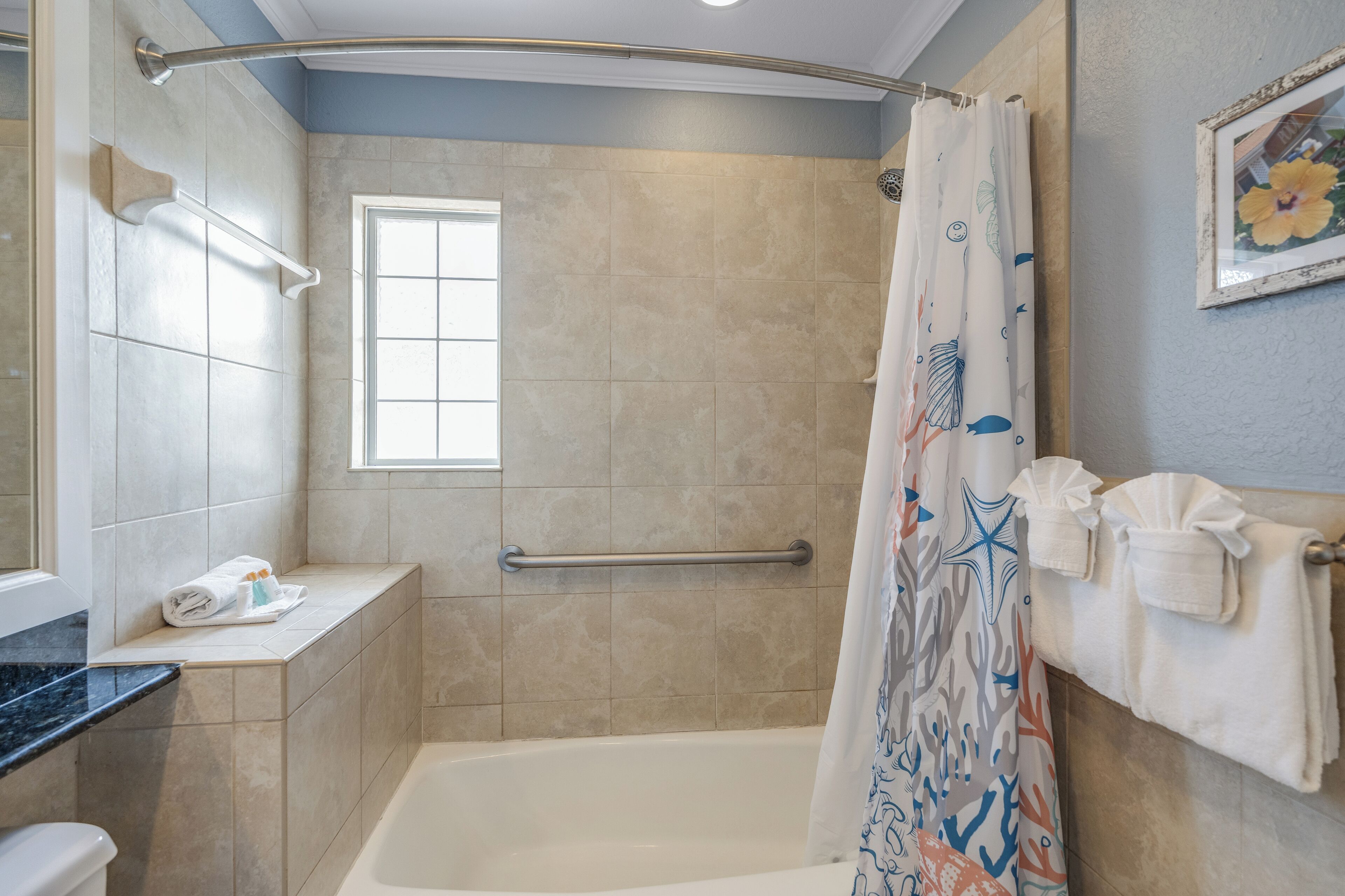 A bathroom with a bathtub, a shower with a curtain, a window, and a towel rack with towels.