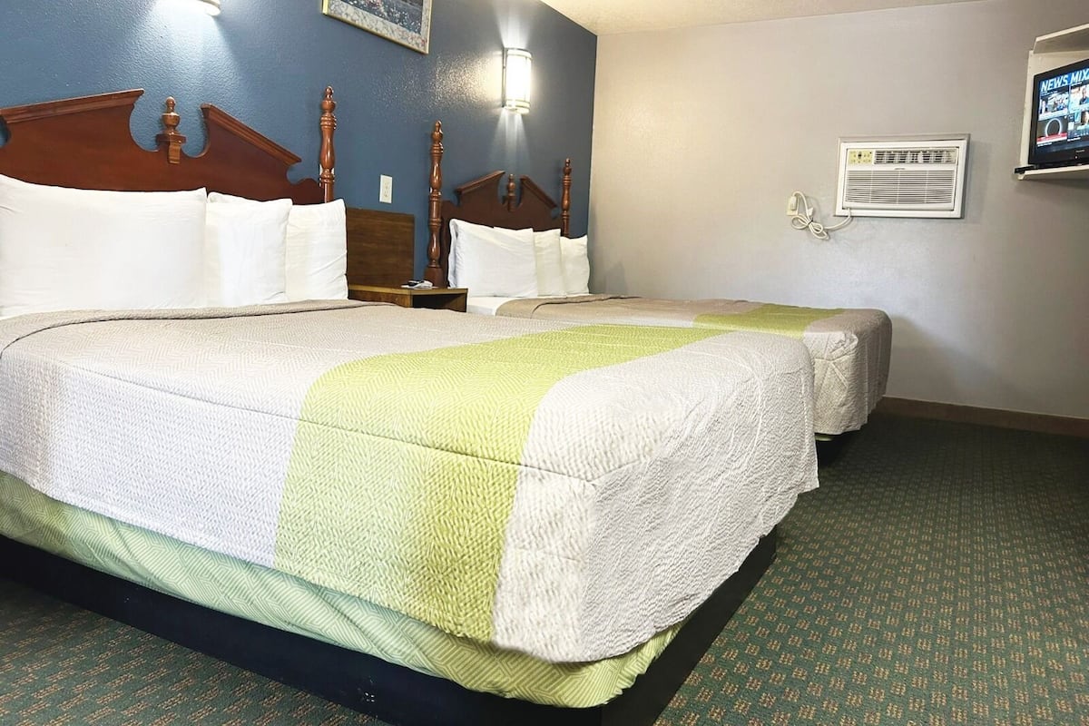 Una habitació d'hotel amb dos llits, una tauleta de nit, un televisor fixat a la paret i un quadre amb marc.