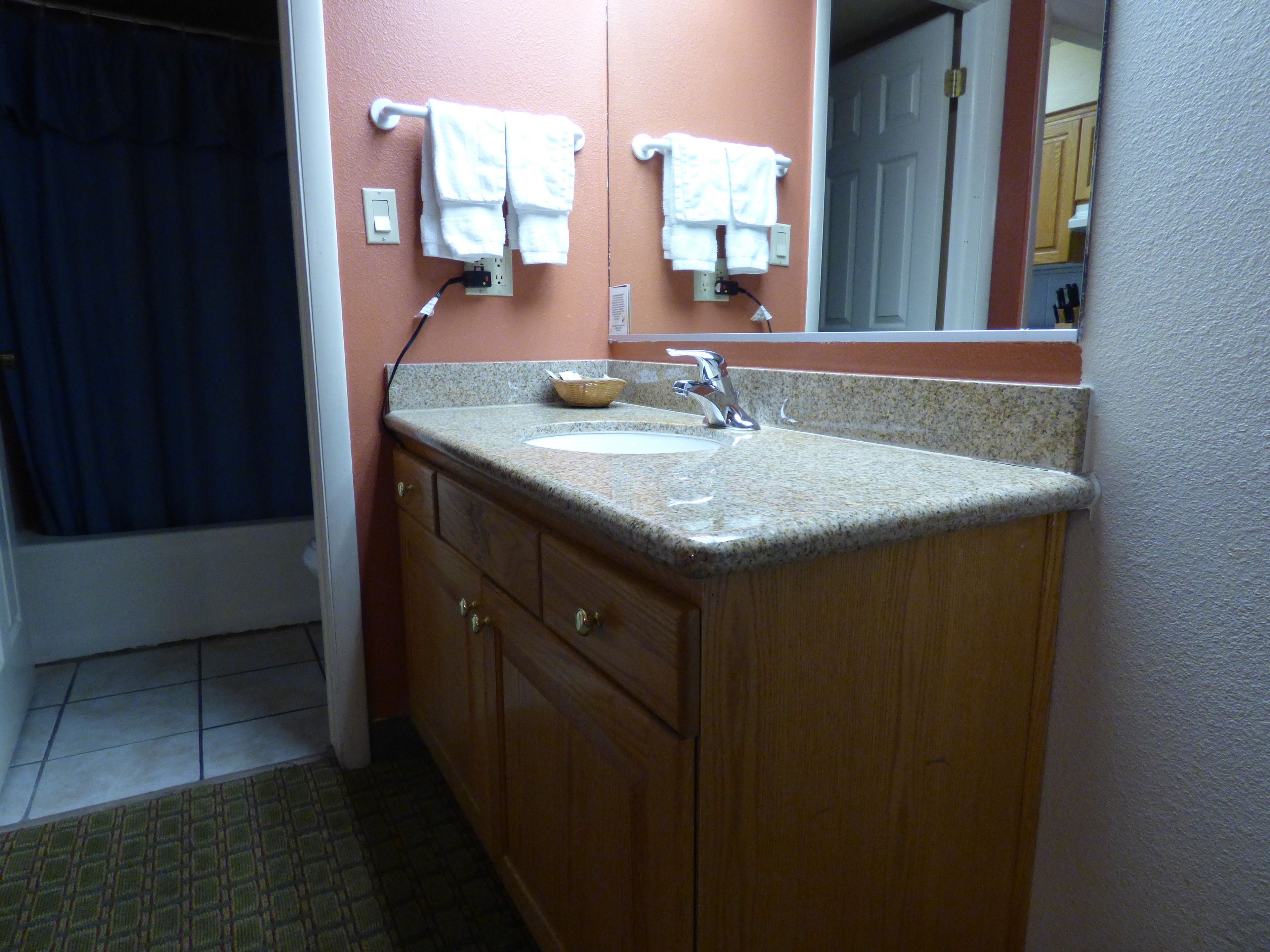 A bathroom with a granite countertop sink, wooden cabinets, and a mirror above the sink.