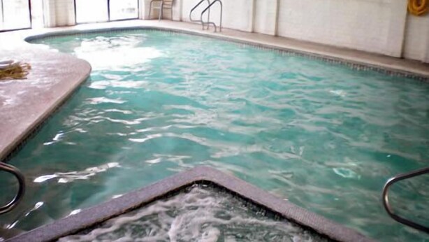 Een binnenzwembad met helder water, een bubbelbadgedeelte en een betegeld zonnedek.