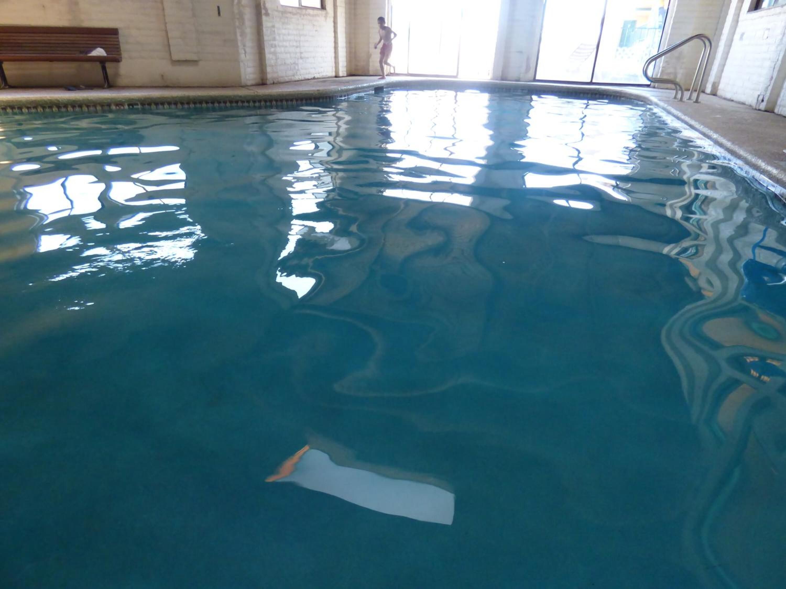 En indendørs swimmingpool med krystalklart vand, en bænk og et barn, der leger.