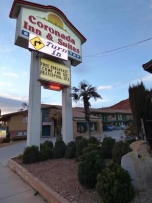 A sign for Coronada Inn & Suites with amenities including free breakfast, complimentary coffee, and a heated pool.