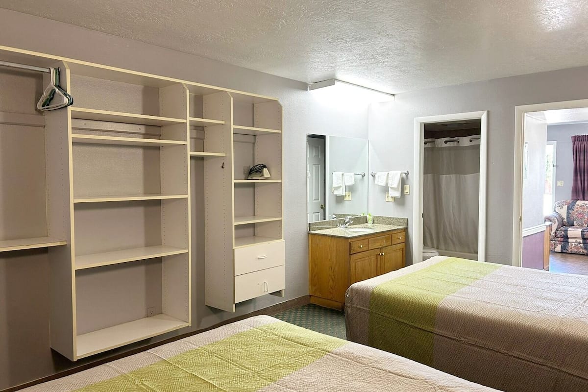 Habitació d'hotel amb dos llits, un tocador de fusta, un mirall gran i un armari amb moltes prestatgeries.