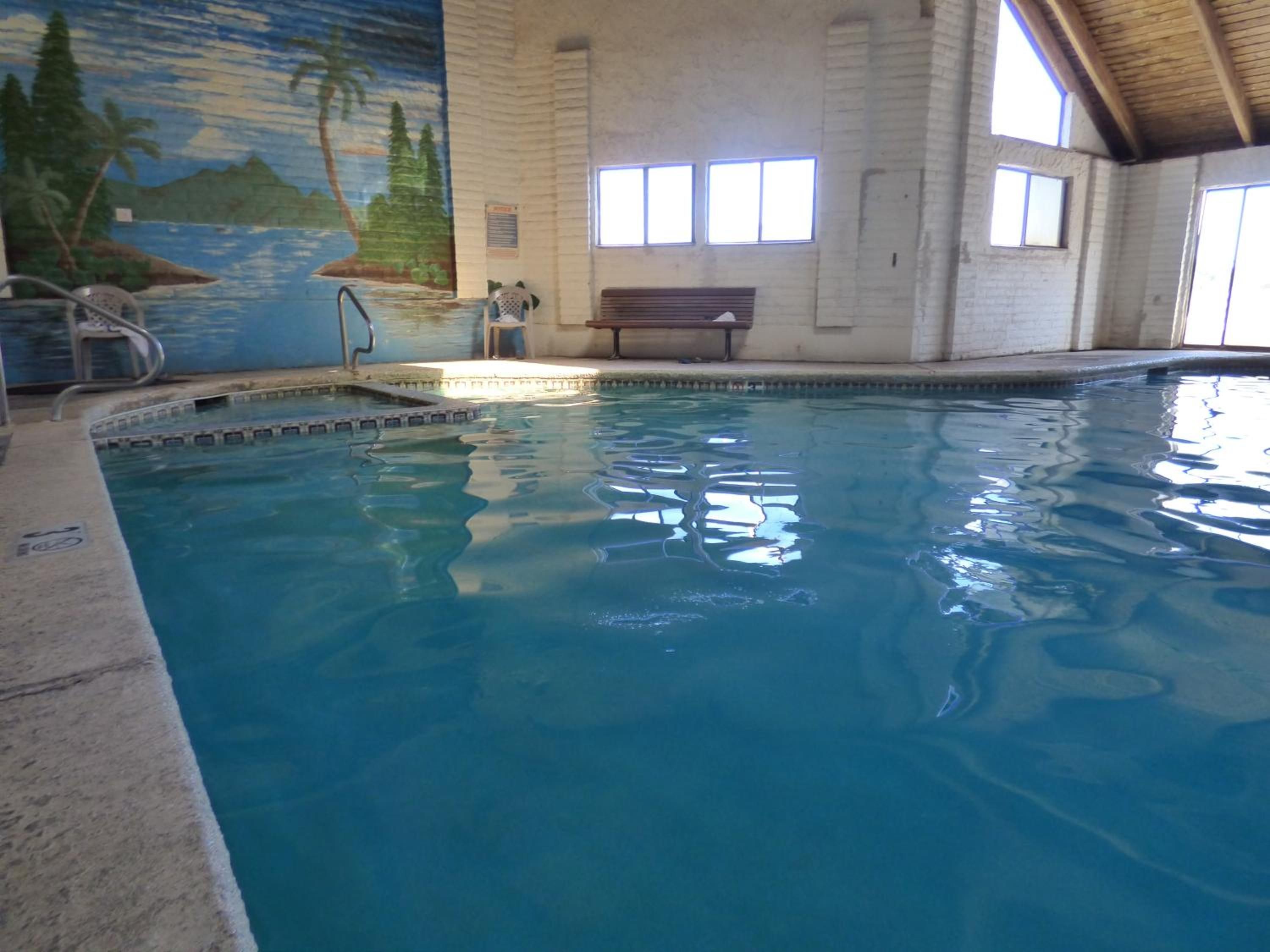 An indoor swimming pool with clear water, a mural on the wall, and a bench.
