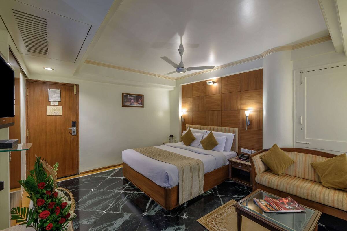Ein Hotelzimmer mit einem Bett, einer Couch, einem Couchtisch, einem Deckenventilator und einem Holzkopfteil.
