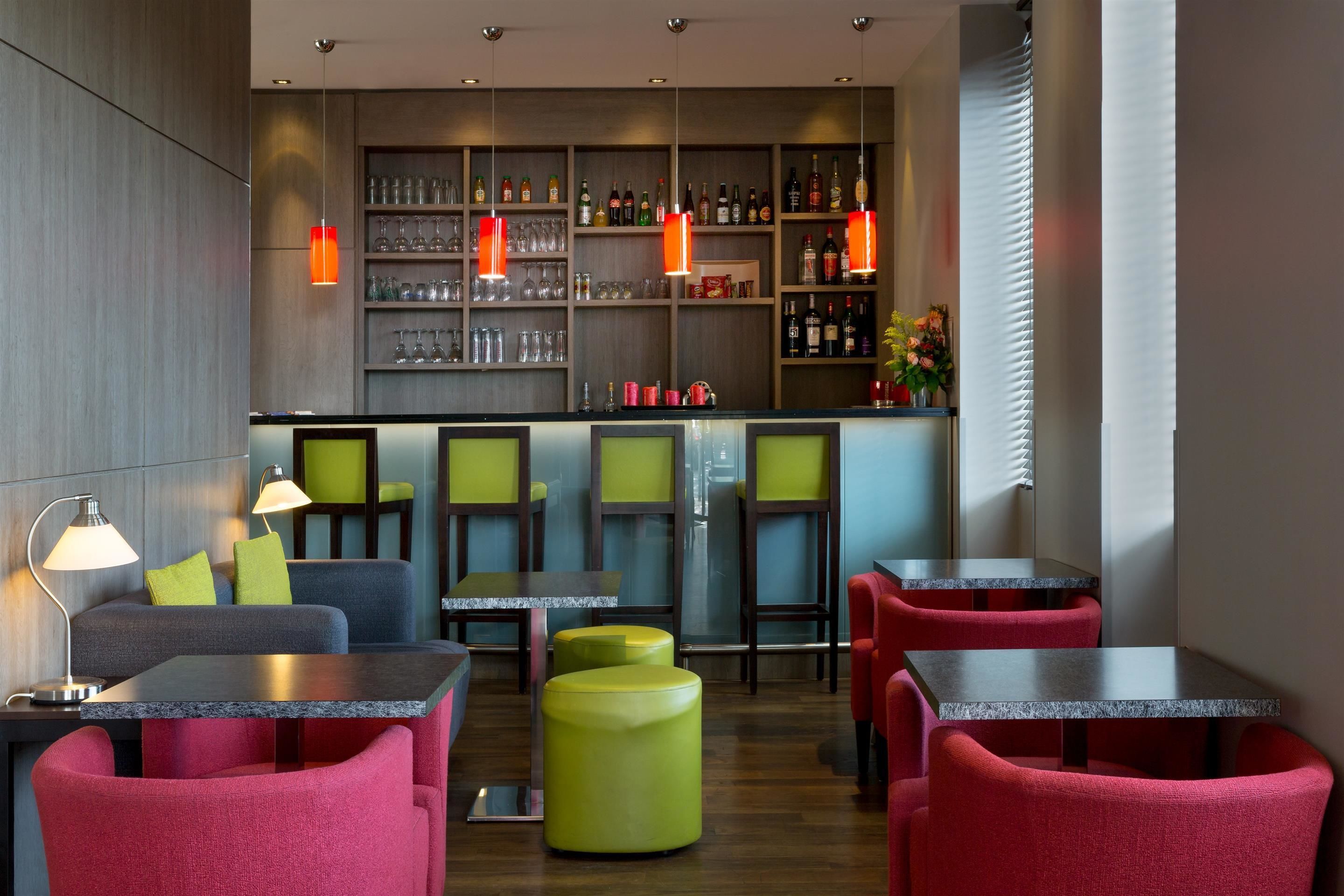 Un espace bar moderne, doté de sièges, d’étagères remplies de bouteilles et de luminaires suspendus.