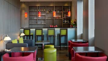 Un espace bar moderne, doté de sièges, d’étagères remplies de bouteilles et de luminaires suspendus.