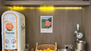 A kitchen counter with a water dispenser, a basket of citrus fruits, a mixing bowl, a juicer, and a cutting board.