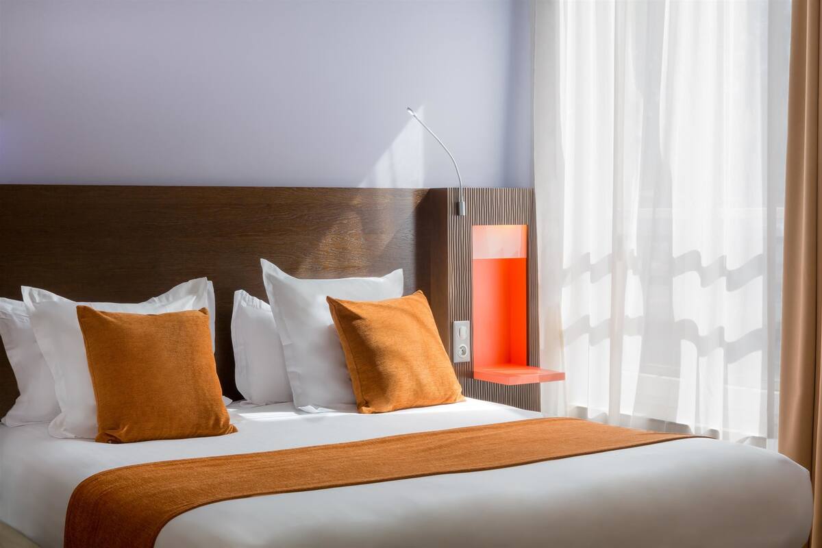 A hotel room with a large bed, white bedding, and a wooden headboard.