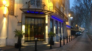 L’entrée d’un hôtel avec une façade en verre, des places assises à l’extérieur et un balcon illuminé de lumière bleue.