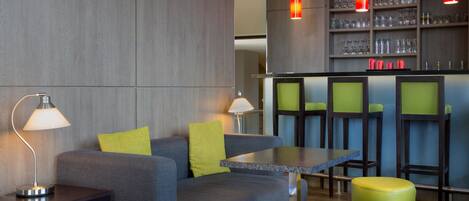 A modern bar area with a sofa, tables, and stools.