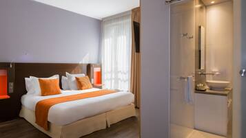 A modern hotel room with a large bed, a shower, and a bathroom with a sink and mirror.