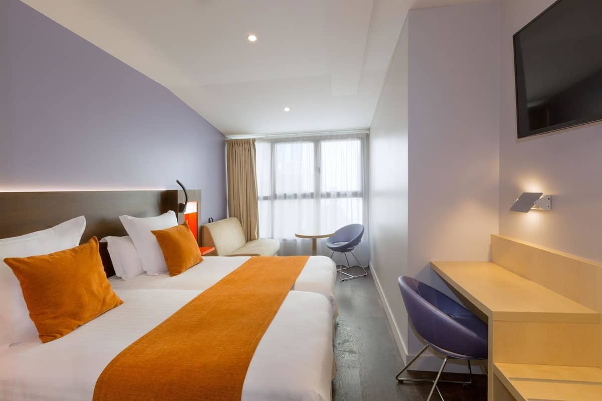 A hotel room with two beds, a desk, a chair, a TV, and a window with curtains.