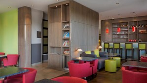 Un espace bar moderne avec des sièges rouges et verts, une bibliothèque et un comptoir avec des verres et des bouteilles.
