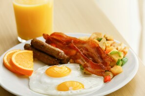 A breakfast plate with eggs, bacon, sausages, and a side of fruit.