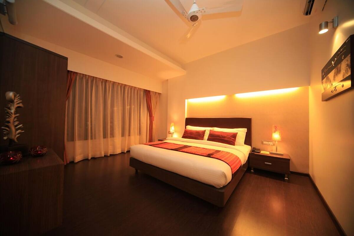 A hotel room with a large bed, a nightstand, a ceiling fan, and a window with curtains.