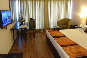 Habitación de hotel con cama, escritorio con silla, una mesita y televisor en la pared.