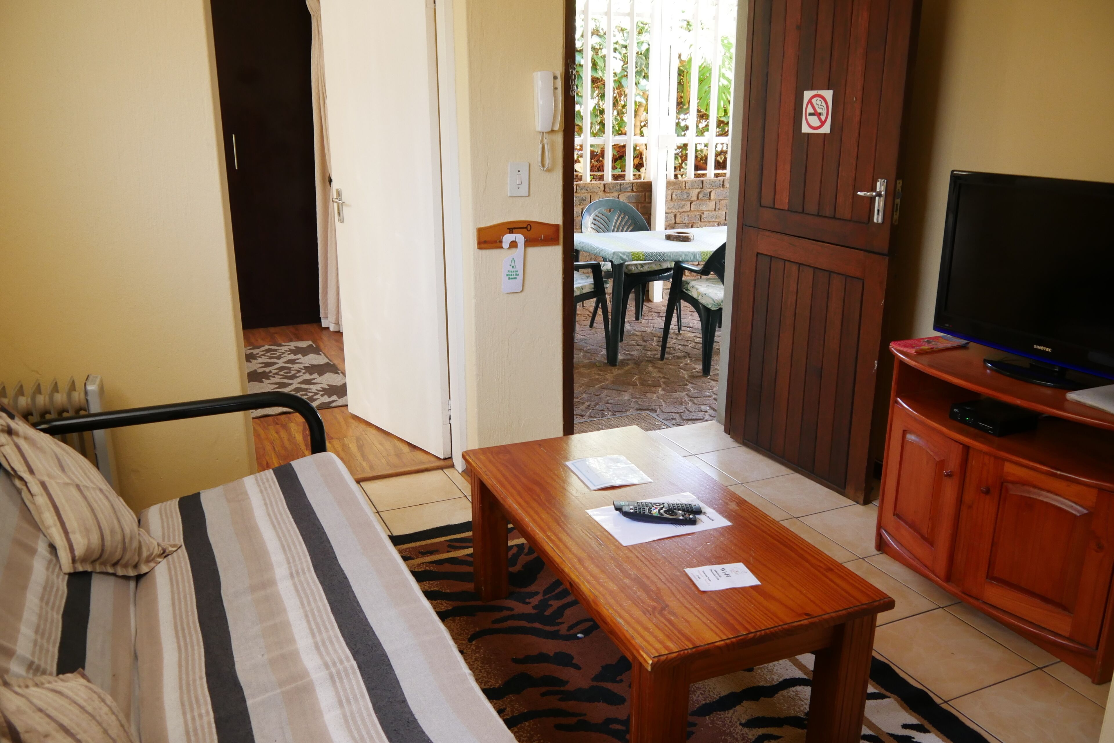 A room with a bed, a wooden table, a television, and a view of an outdoor patio area.