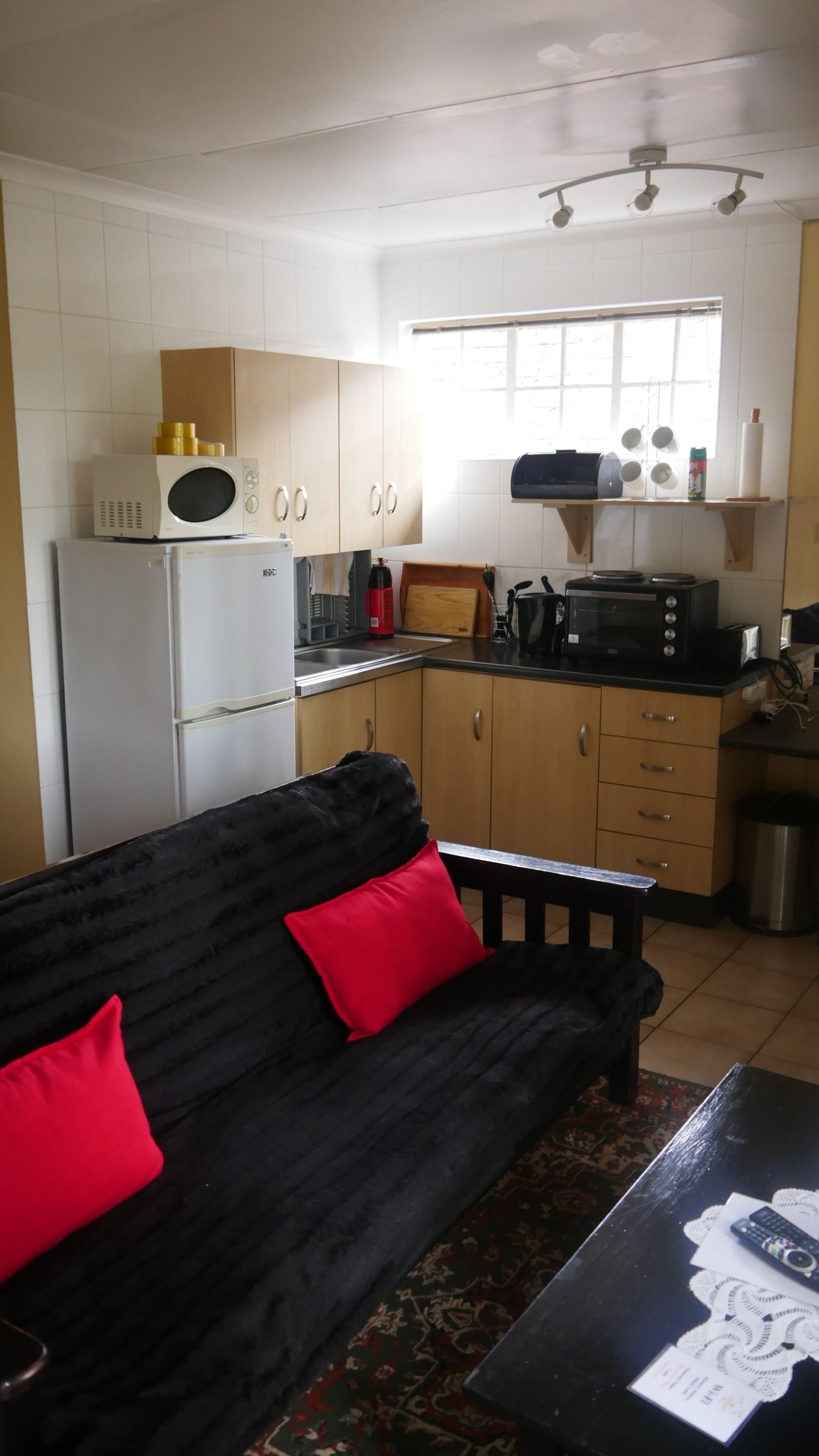 A compact kitchen with white cabinets, a black microwave, a toaster, and a small window.