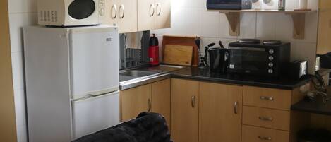 A compact kitchen with white cabinets, a black microwave, a toaster, and a small window.