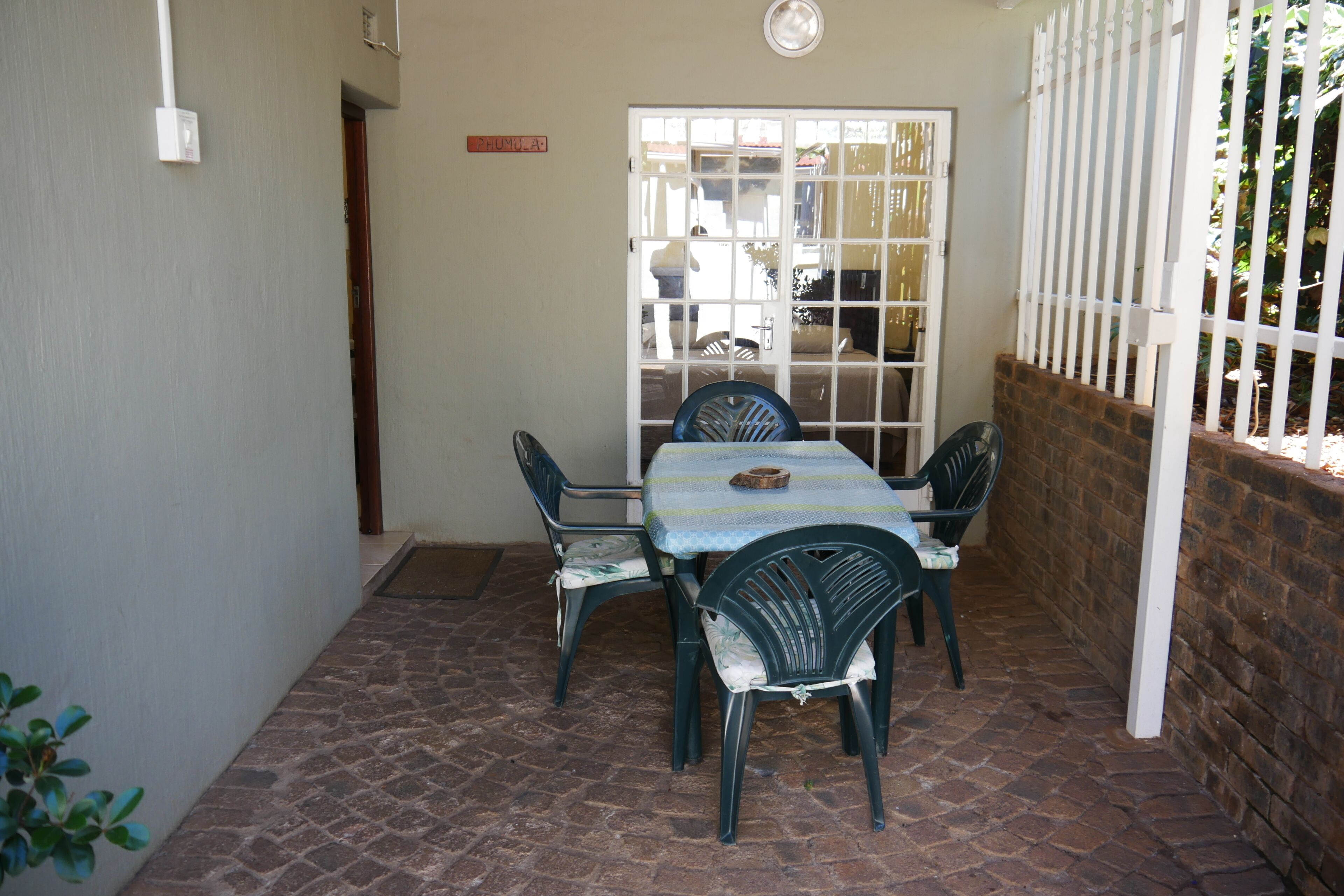 Uma área de pátio com uma mesa e quatro cadeiras, uma porta branca e um muro de tijolos.