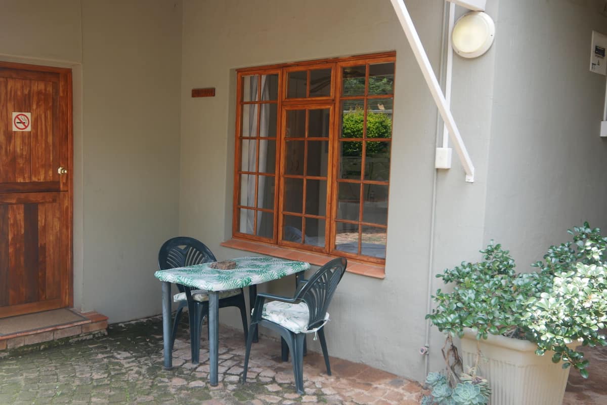 Un pequeño espacio al aire libre con una mesa y dos sillas, una puerta de madera y una ventana con vistas a la vegetación.