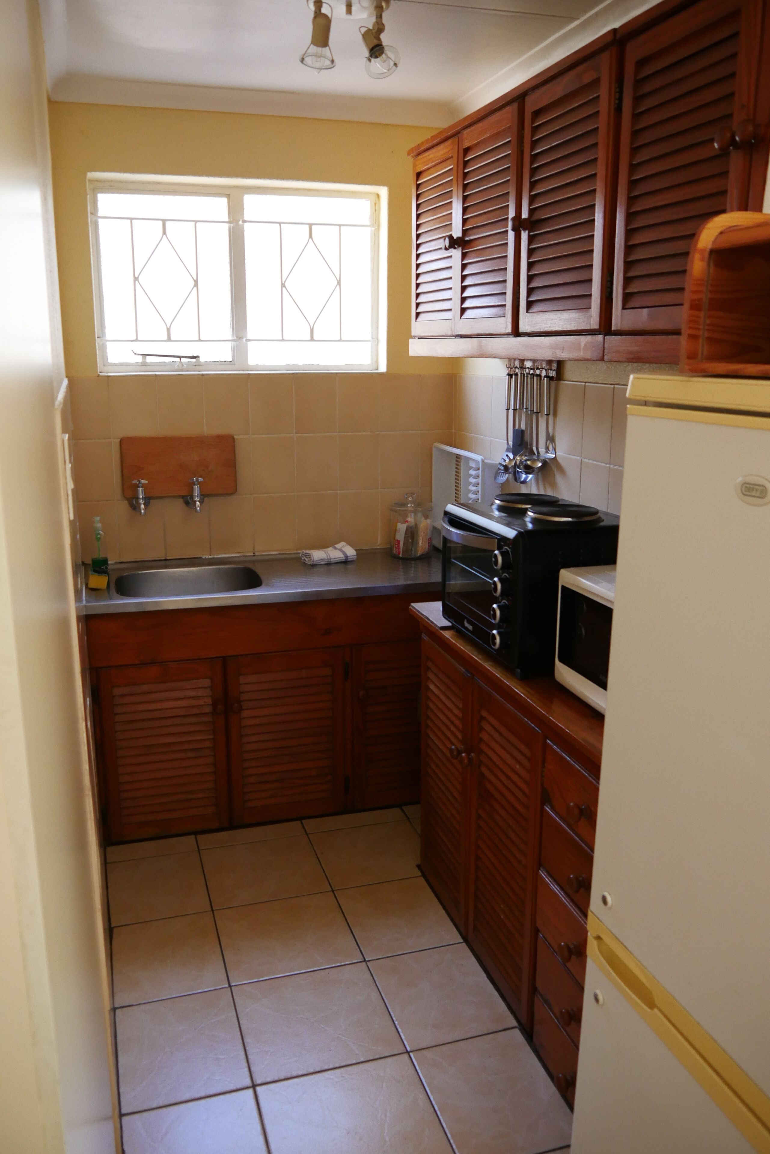 A compact kitchen with wooden cabinets, a built-in oven, a microwave, and a sink.