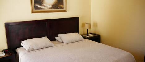 Una cama bien hecha con un cabecero, una mesita de noche con una lámpara y un cuadro enmarcado en la pared.