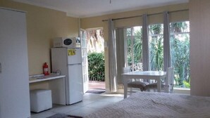 Een knus verblijf met een bed, een kitchenette met een magnetron, een klein tafeltje en uitzicht op groen via een schuifdeur.