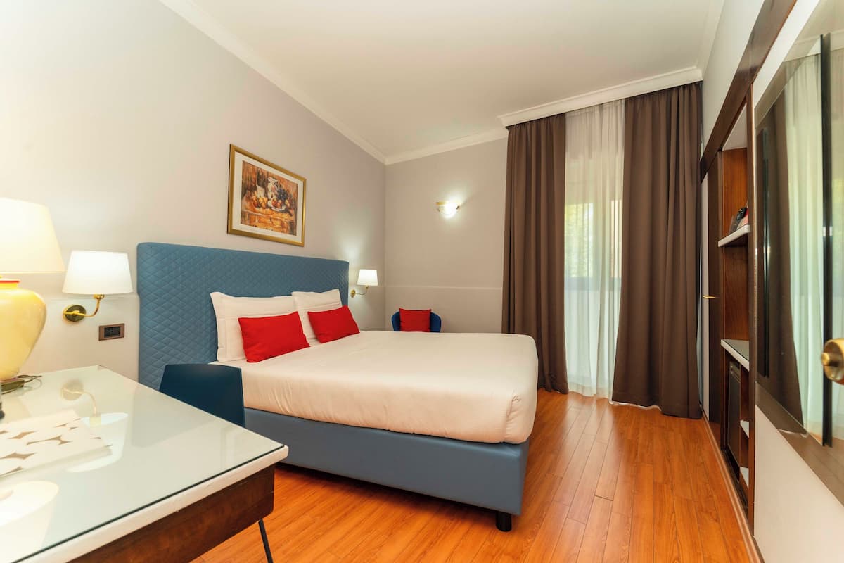 A hotel room with a bed, bedside table, lamp, and a painting on the wall.