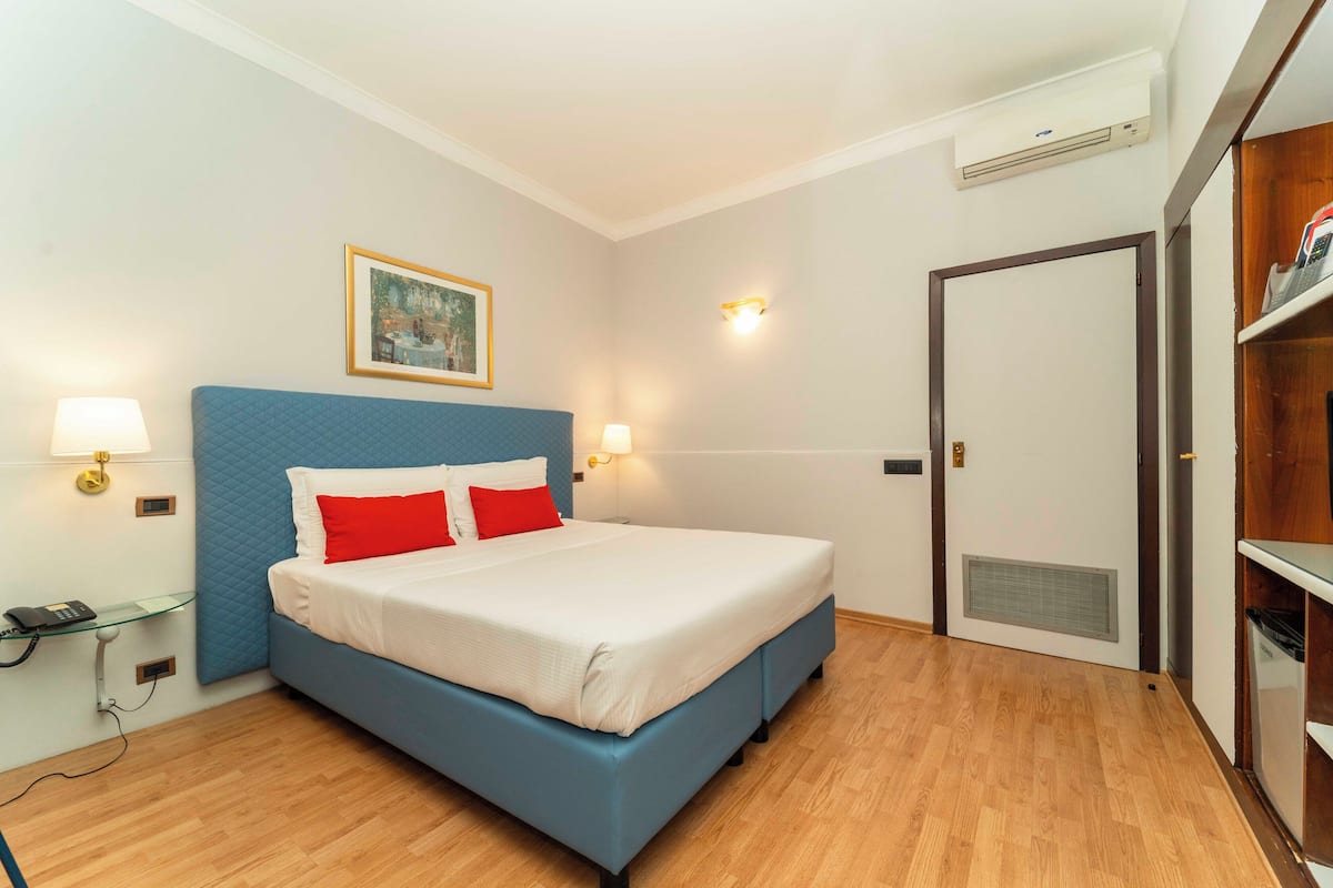 A bedroom with a bed, bedside lamps, a painting, and a wardrobe.