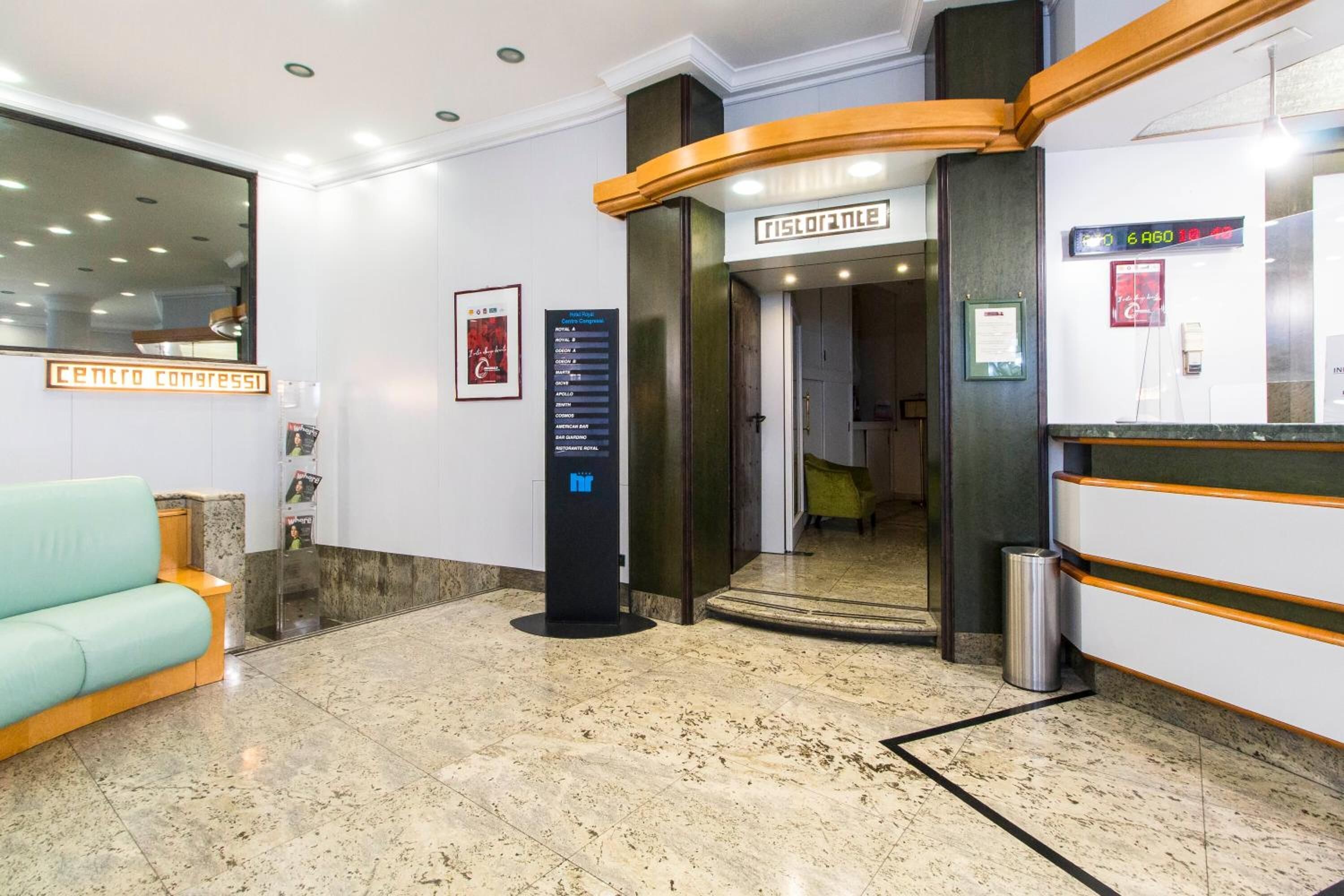 Un vestíbulo con una recepción, una zona de espera con un sofá color turquesa, un reloj digital y un letrero de directorio.