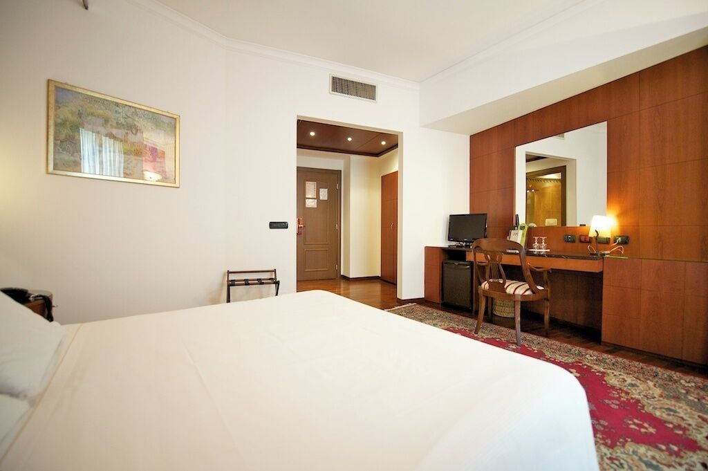 Ein Hotelzimmer mit einem großen Bett, einem Schreibtisch mit Stuhl, einem Fernseher und einem Spiegel.