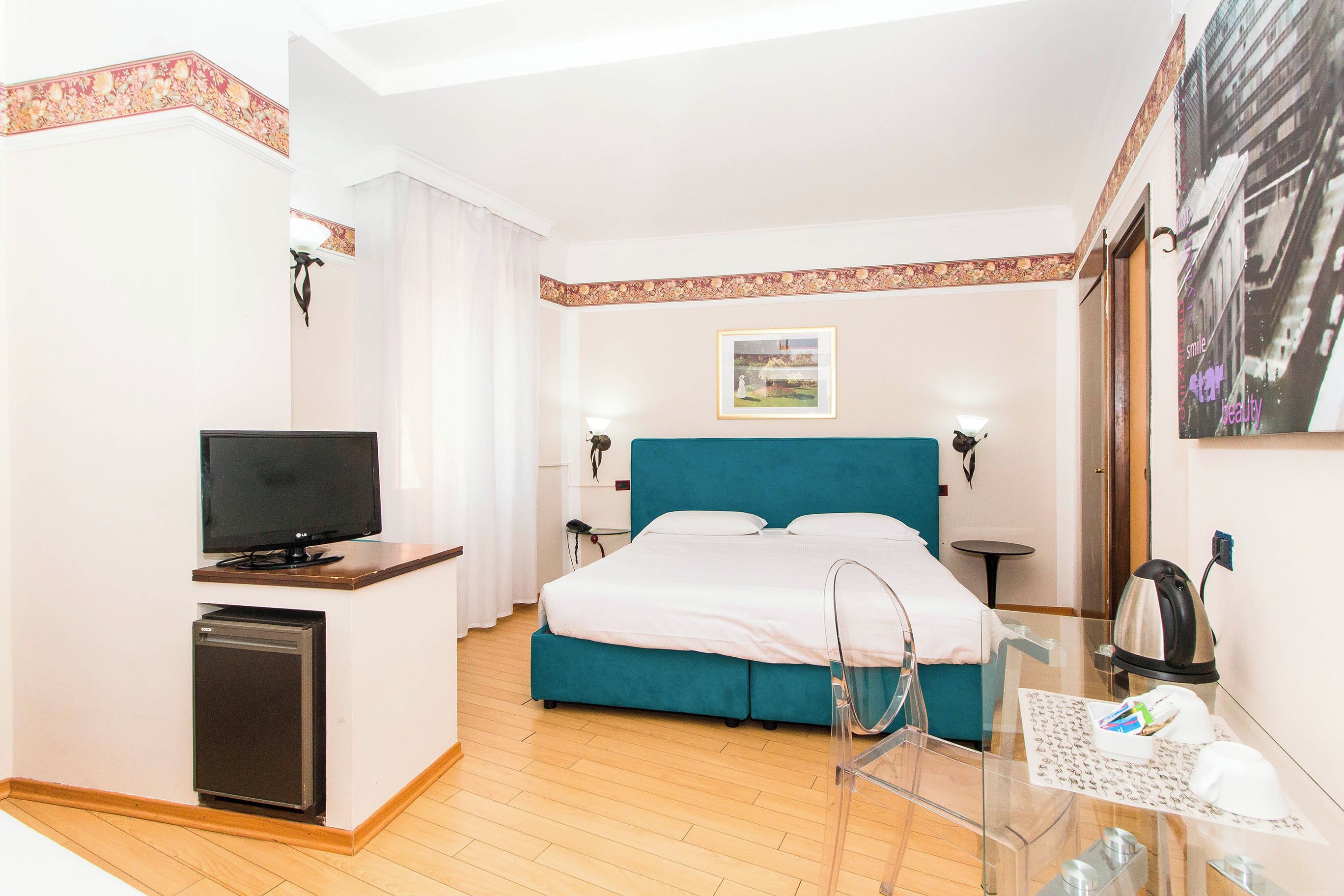 A hotel room with a bed, a TV, a desk, and a small fridge.