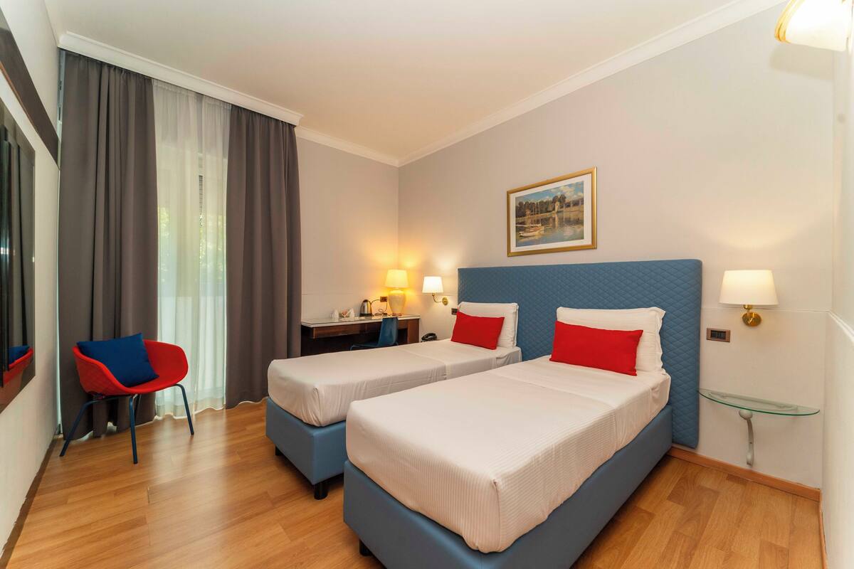 A hotel room with two beds, a desk, a chair, and a glass table.