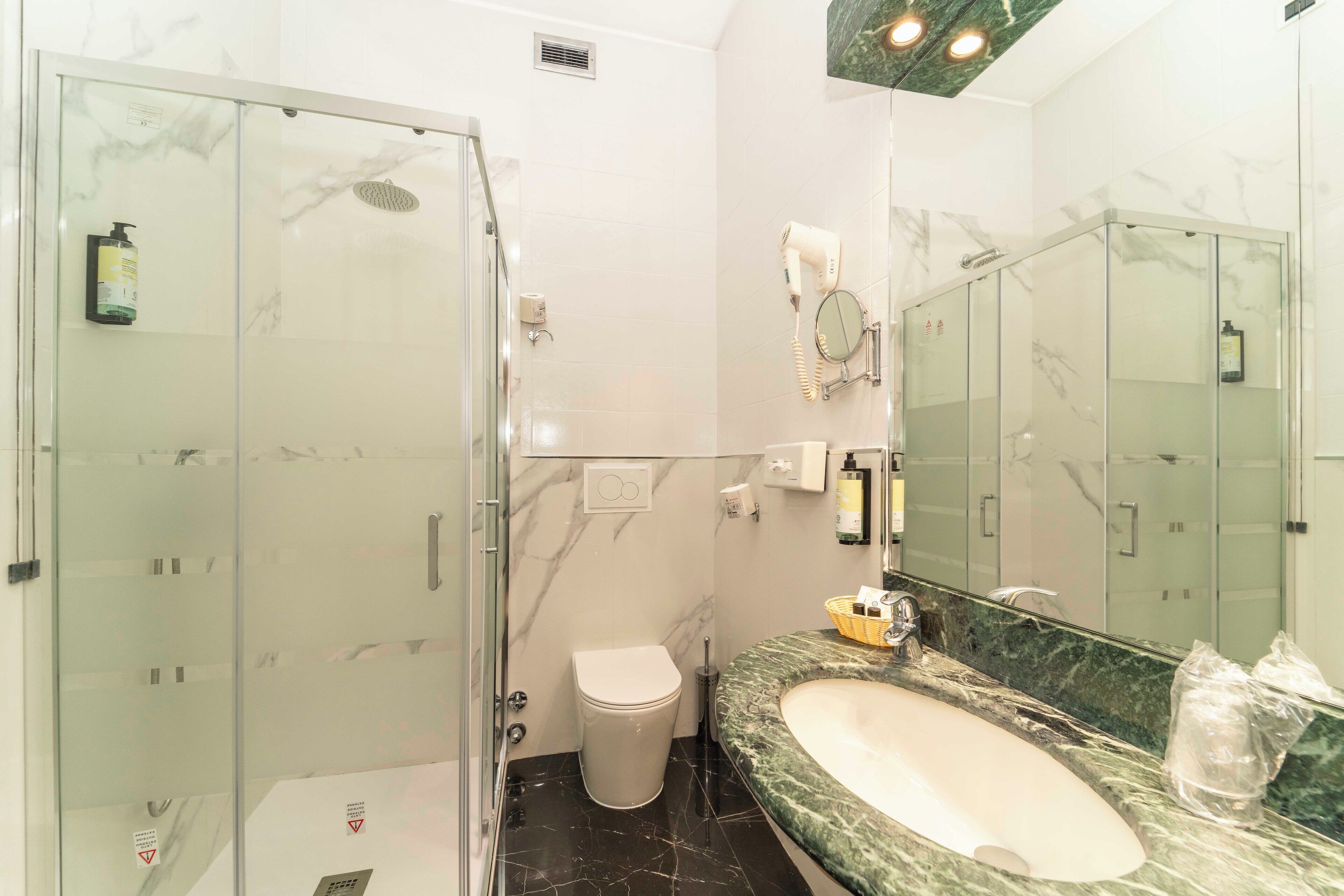 Un baño moderno con cabina de ducha de vidrio, lavamanos de mármol y un espejo grande.