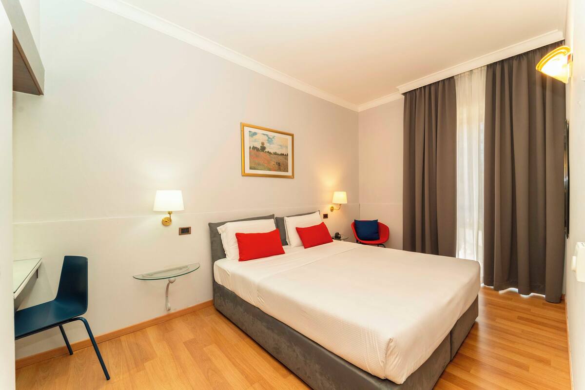 A hotel room with a bed, a desk, a chair, and a small table.
